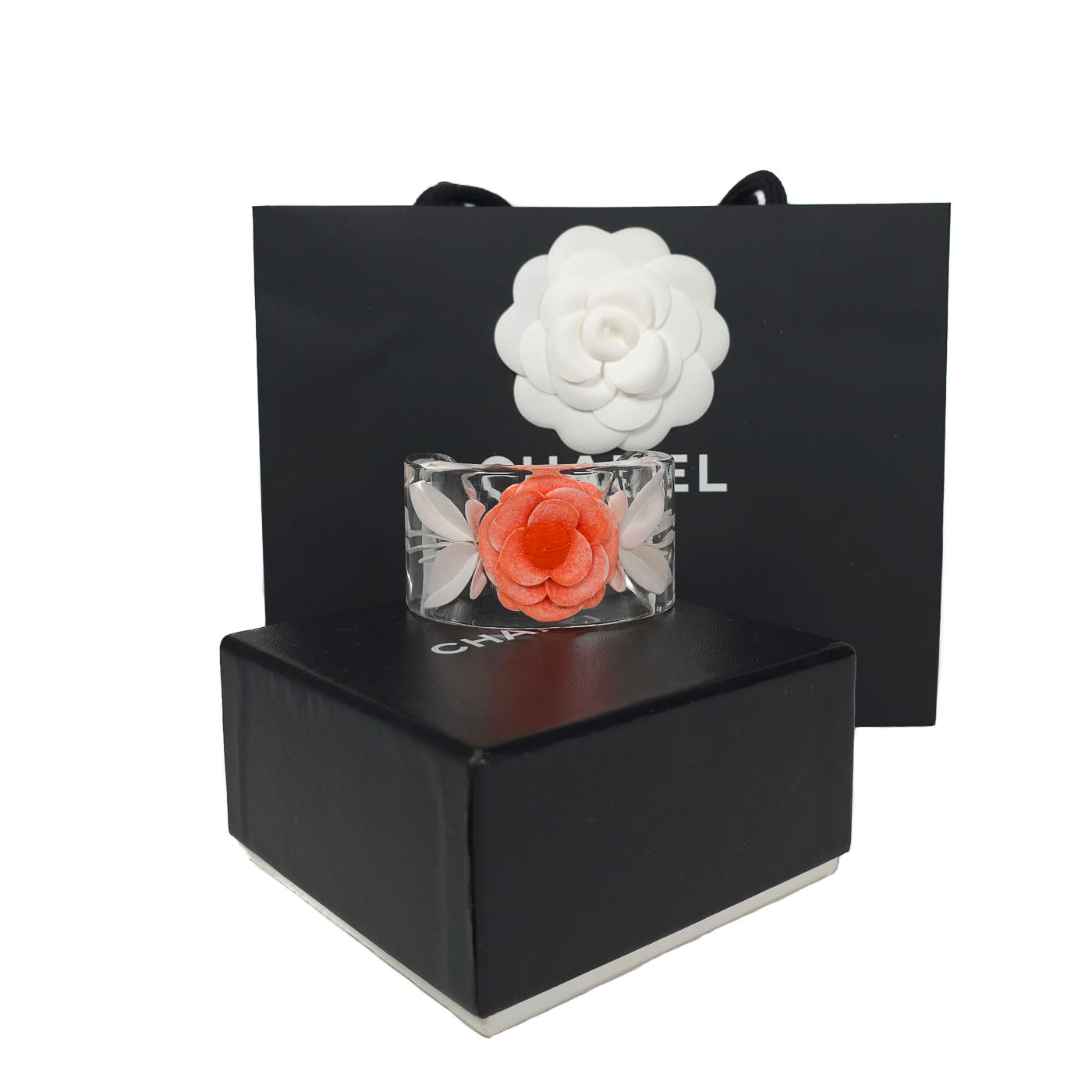 A vintage Chanel coral camellia flower lucite resin cuff bracelet displayed on a black box with the Chanel brand visible, y2k.