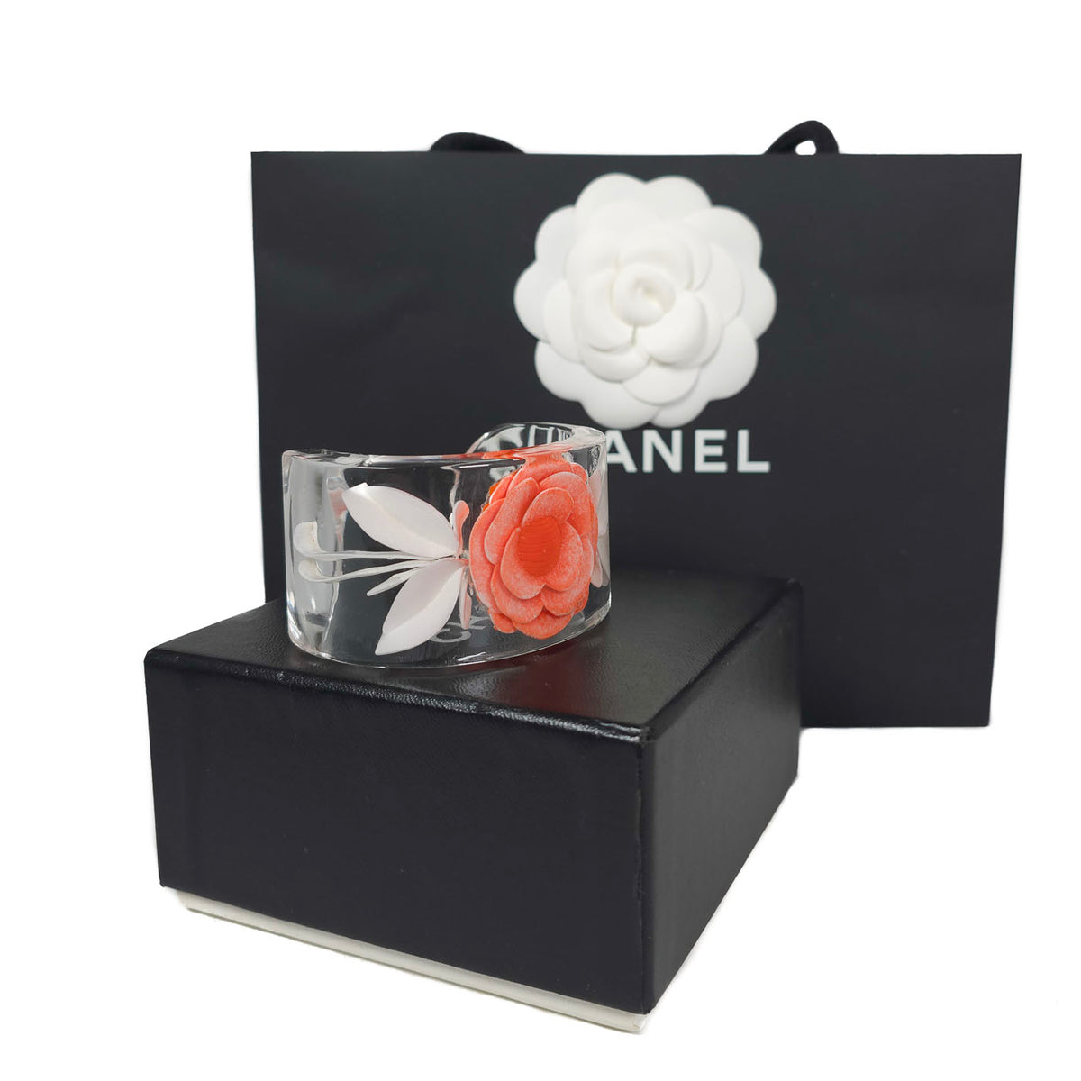 A vintage Chanel coral camellia flower lucite resin cuff bracelet displayed on a black box with the Chanel brand visible, y2k.