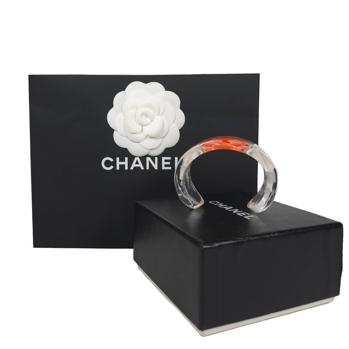 A vintage Chanel coral camellia flower lucite resin cuff bracelet displayed on a black box with the Chanel brand visible, y2k.
