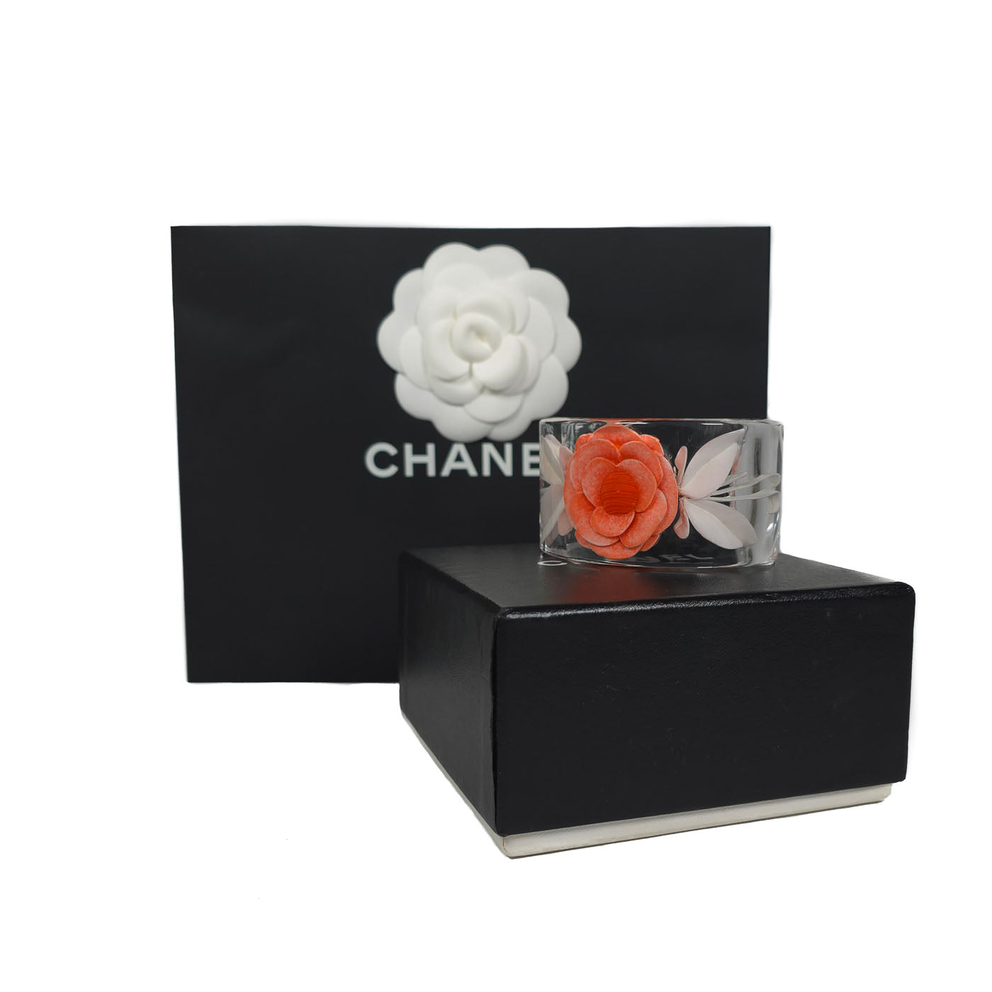 A vintage Chanel coral camellia flower lucite resin cuff bracelet displayed on a black box with the Chanel brand visible, y2k.