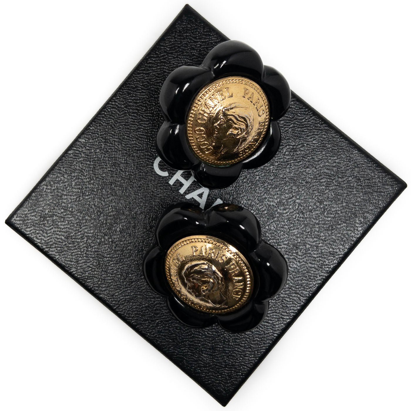 Vintage Chanel Earrings Black Camelia Coco Cameo Clip 1984
A pair of vintage Chanel black camellia clip earrings featuring a golden cameo design.