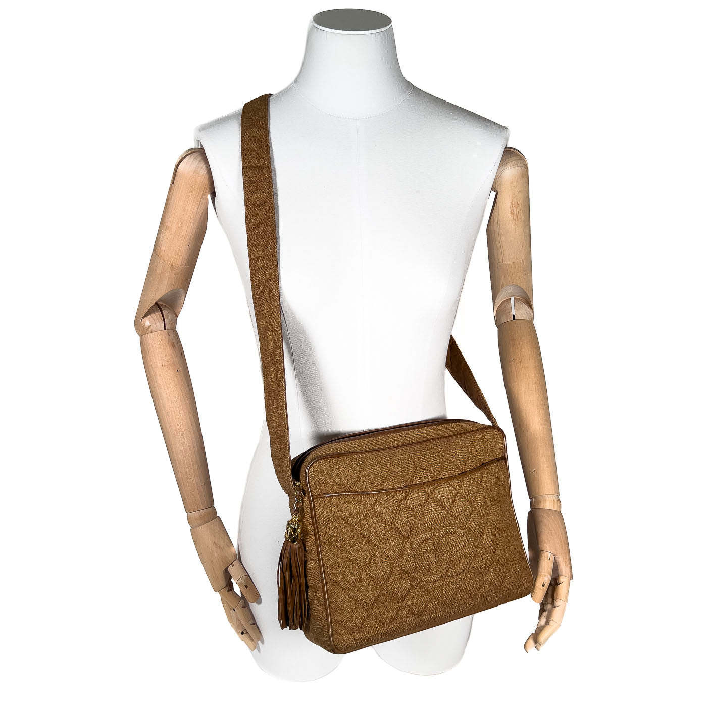 A vintage Chanel camera bag in camel brown with a quilted design, large stitched CC logo, and a tassel. Displayed on a mannequin.