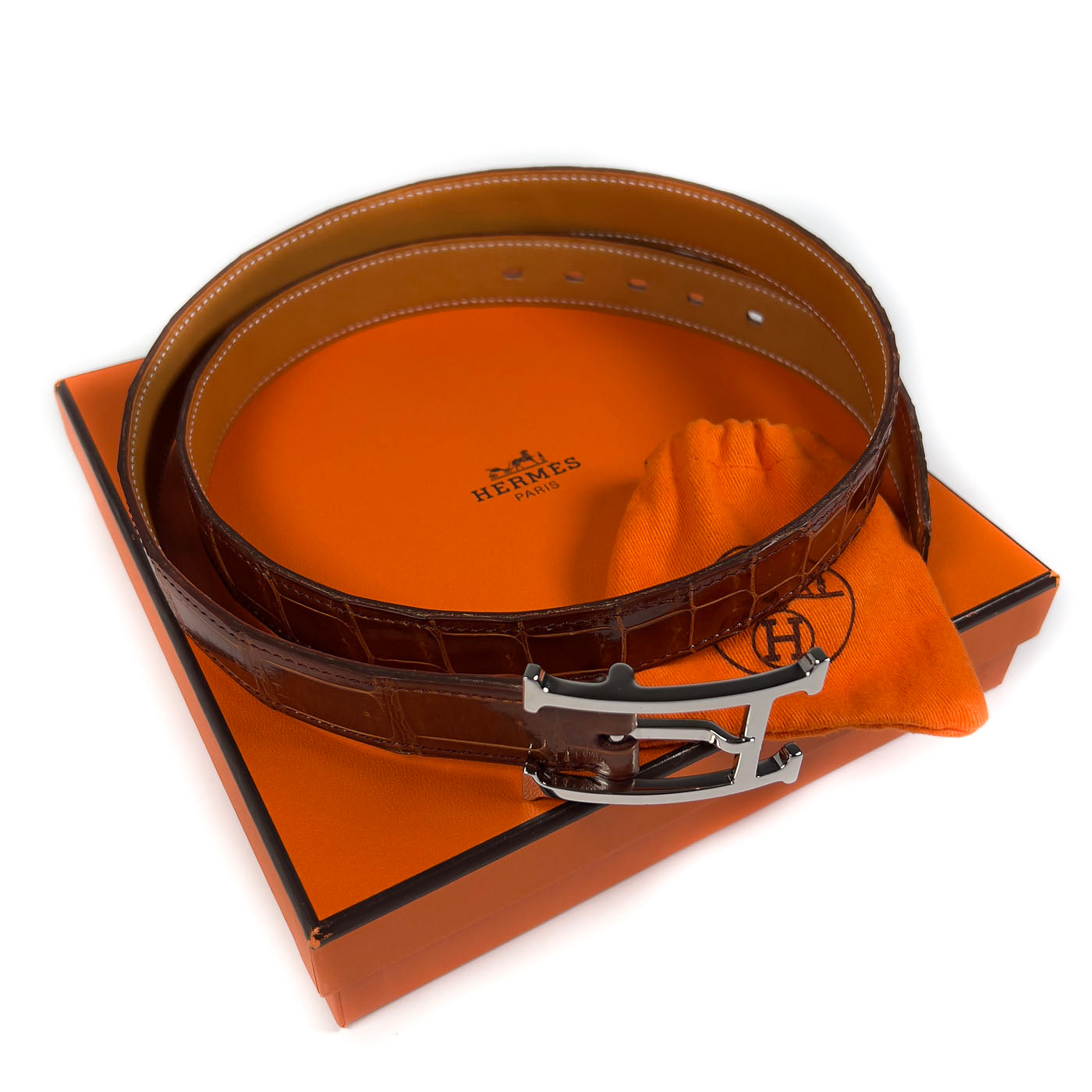 Pre-owned Hermès Cognac Porosus Crocodile Belt with Palladium Hardware Size 90, displayed on a white surface with an orange cloth.