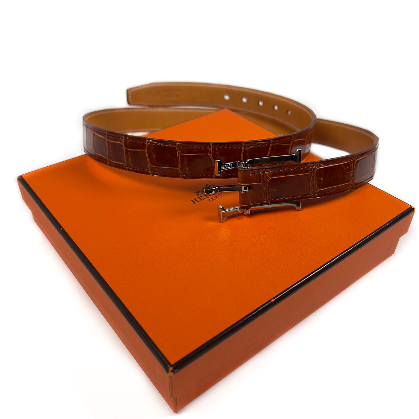 Pre-owned Hermès Cognac Porosus Crocodile Belt with Palladium Hardware Size 90, displayed on a white surface with an orange cloth.