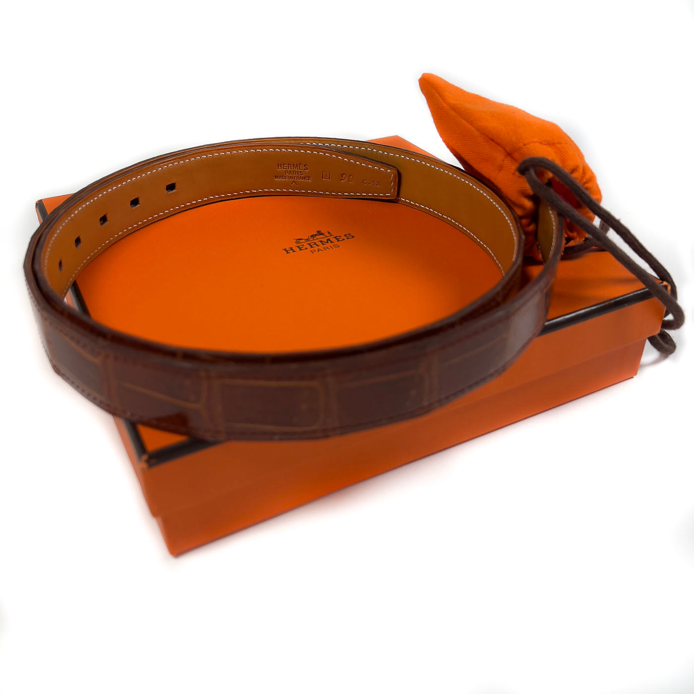 Pre-owned Hermès Cognac Porosus Crocodile Belt with Palladium Hardware Size 90, displayed on a white surface with an orange cloth.