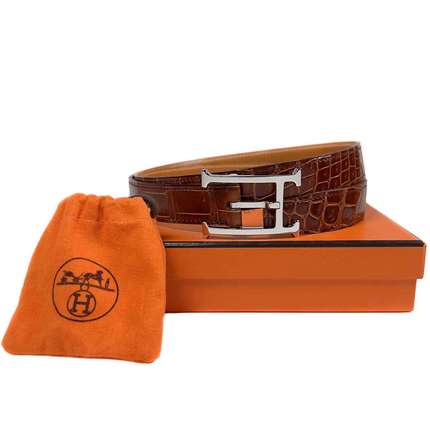 Pre-owned Hermès Cognac Porosus Crocodile Belt with Palladium Hardware Size 90, displayed on a white surface with an orange cloth.